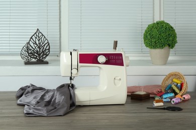 Sewing machine, gray fabric and craft accessories on wooden table indoors