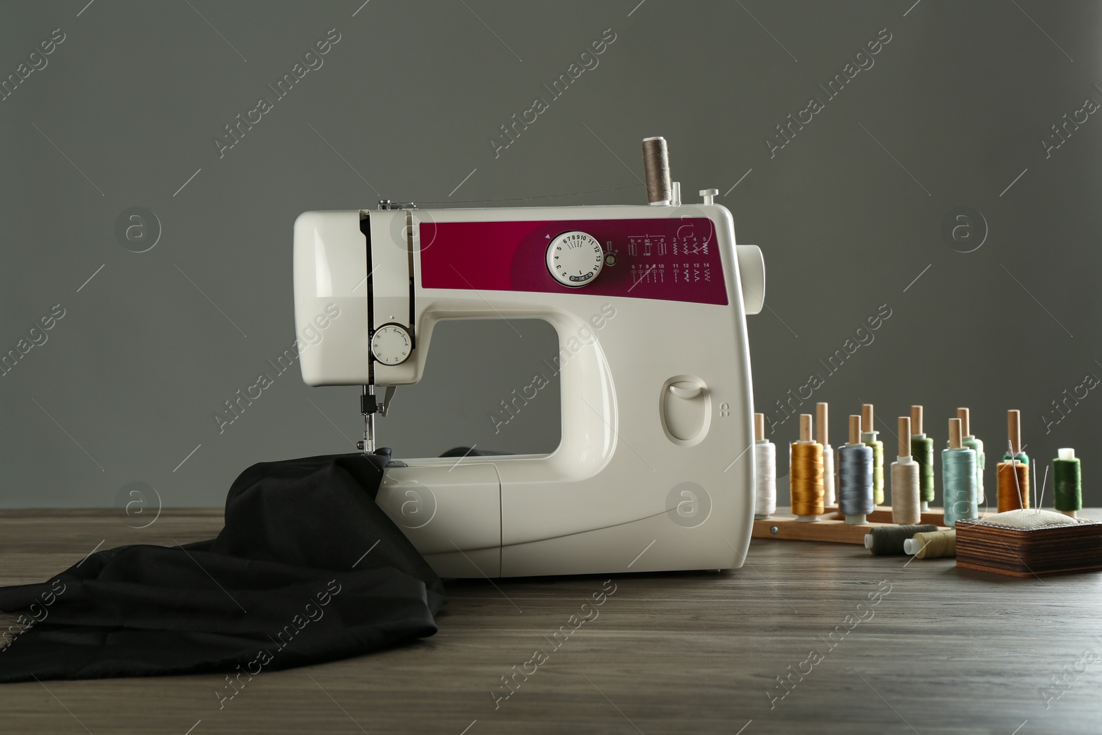 Photo of Sewing machine, black fabric and craft accessories on wooden table against gray background