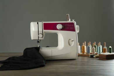 Sewing machine, black fabric and craft accessories on wooden table against gray background