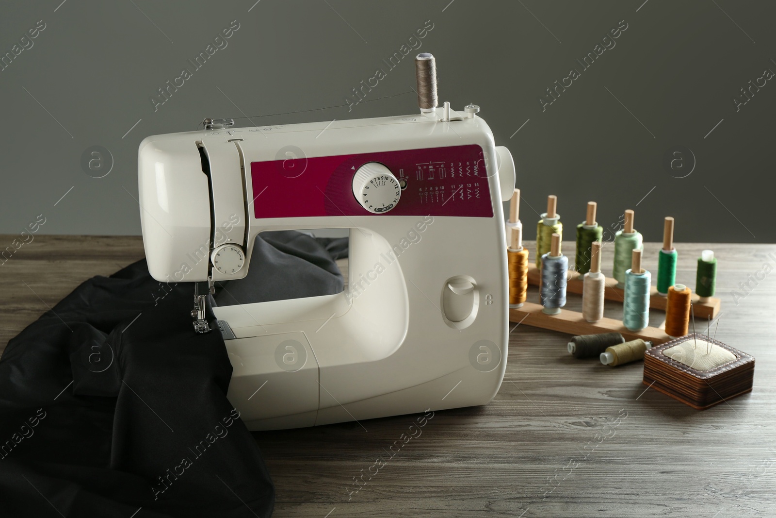 Photo of Sewing machine, black fabric and craft accessories on wooden table against gray background