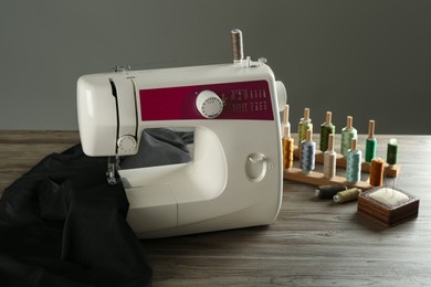 Sewing machine, black fabric and craft accessories on wooden table against gray background