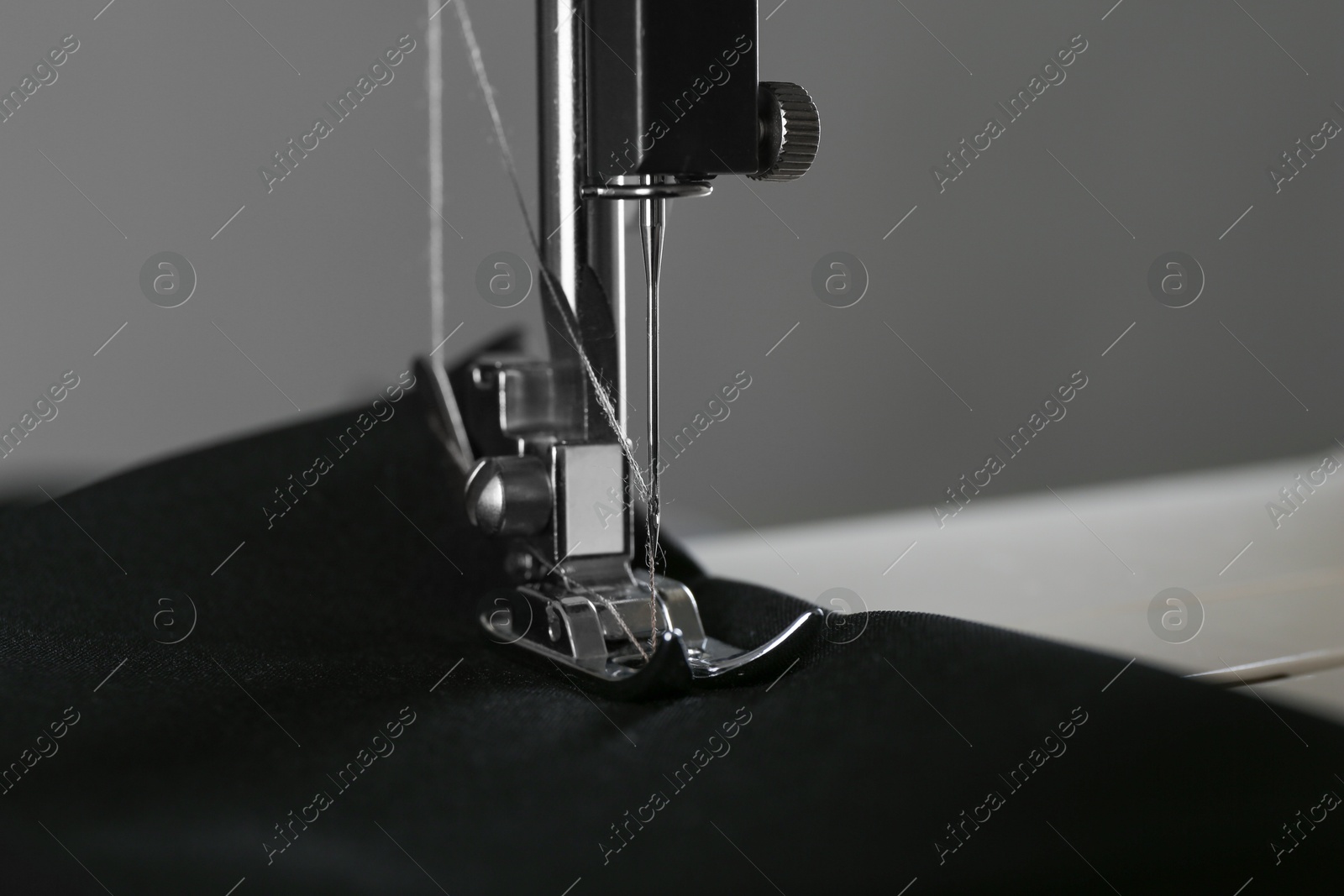 Photo of Sewing machine with black fabric on gray background, closeup