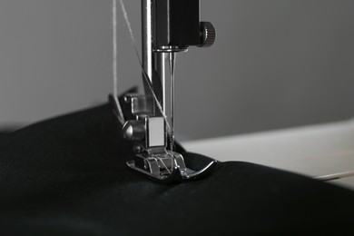 Photo of Sewing machine with black fabric on gray background, closeup