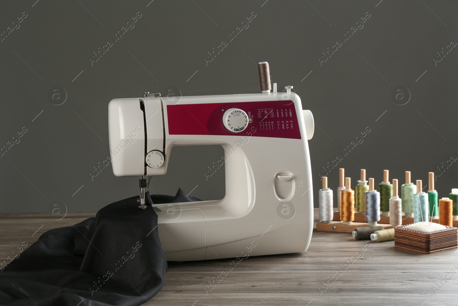 Photo of Sewing machine, black fabric and craft accessories on wooden table against gray background