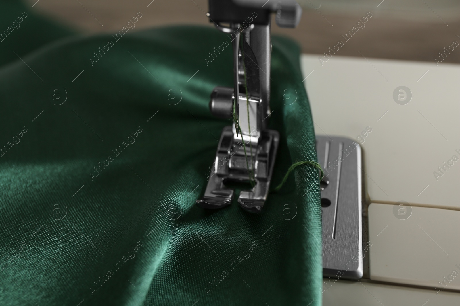 Photo of Sewing machine with green fabric on light background, closeup