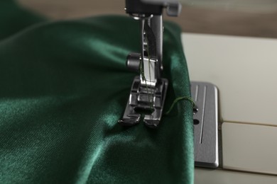 Photo of Sewing machine with green fabric on light background, closeup