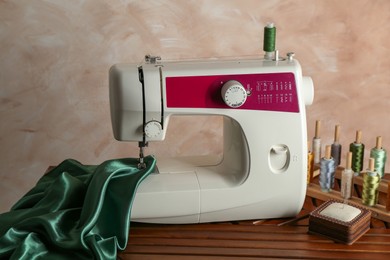 Photo of Sewing machine, green fabric and craft accessories on wooden table indoors