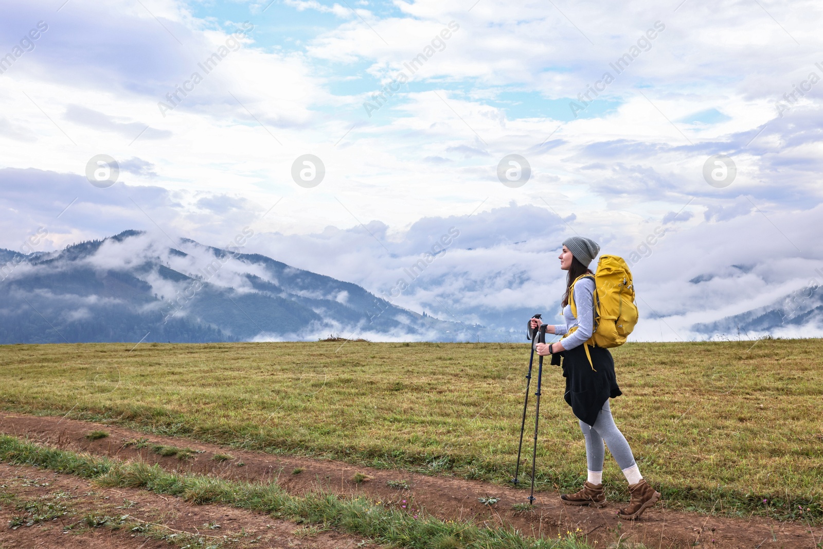 Photo of Young hiker with trekking poles and backpack in mountains outdoors. Space for text