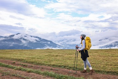 Young hiker with trekking poles and backpack in mountains outdoors. Space for text