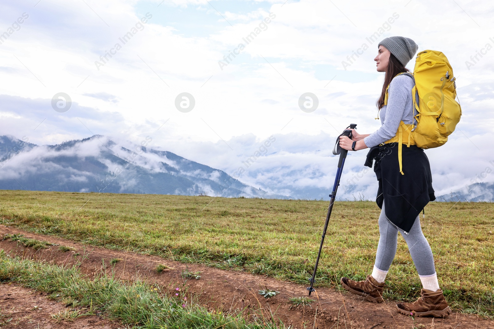 Photo of Young hiker with trekking poles and backpack in mountains outdoors, space for text