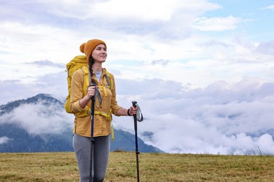 Young hiker with trekking poles and backpack in mountains outdoors, space for text