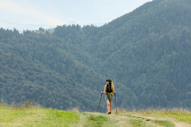 Photo of Young hiker with backpack and trekking poles in mountains, space for text