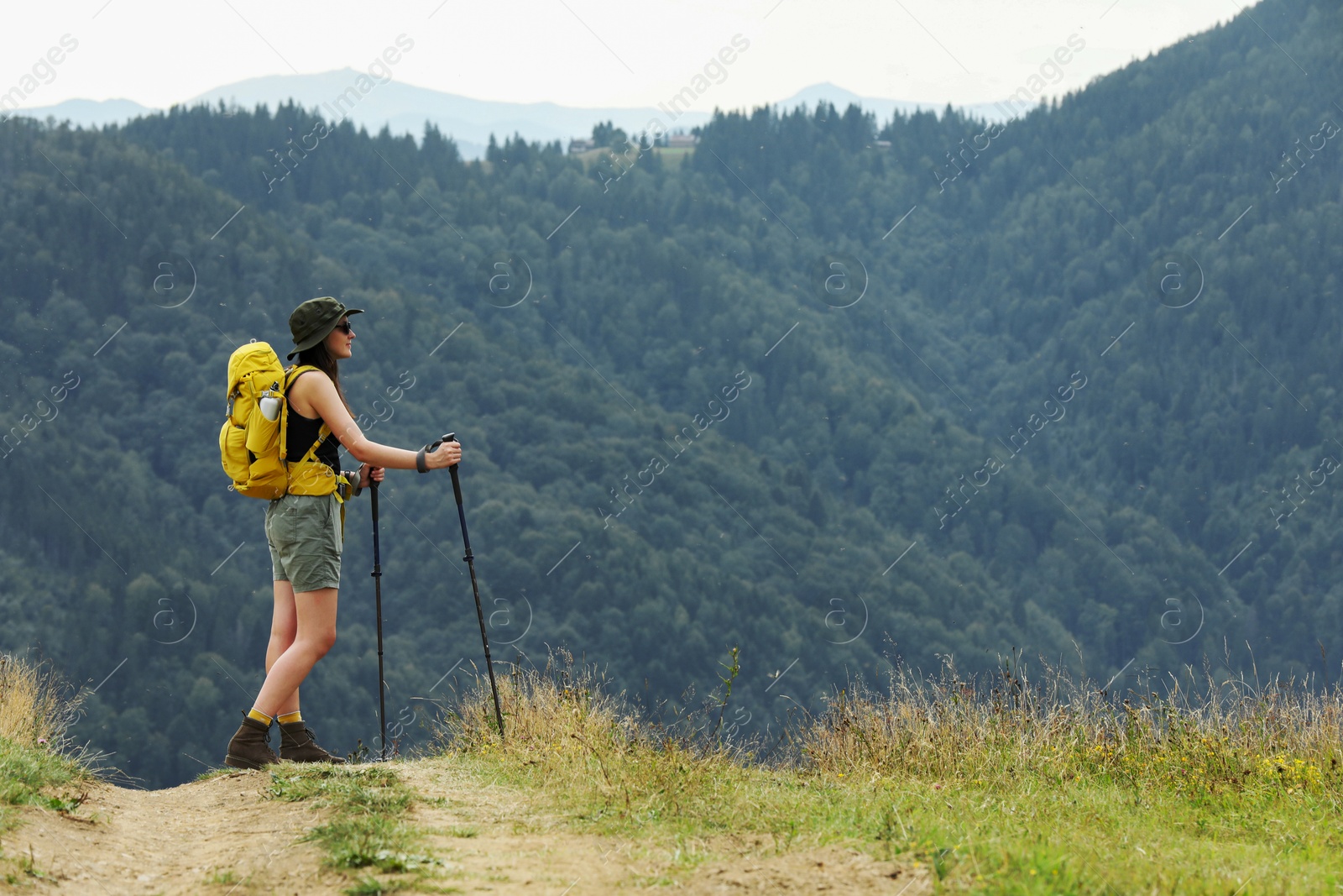 Photo of Young hiker with backpack and trekking poles in mountains, space for text