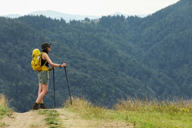 Young hiker with backpack and trekking poles in mountains, space for text