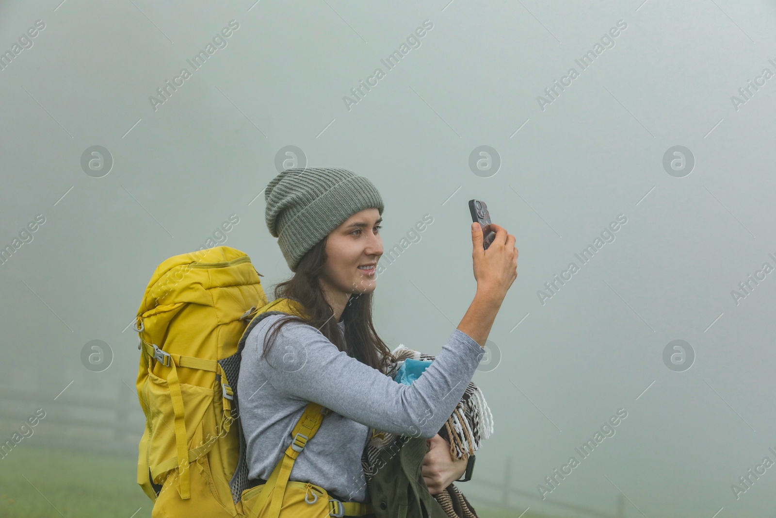 Photo of Young hiker with backpack taking selfie in misty mountains