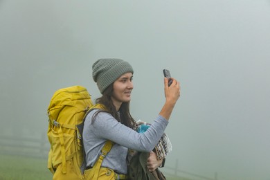 Young hiker with backpack taking selfie in misty mountains