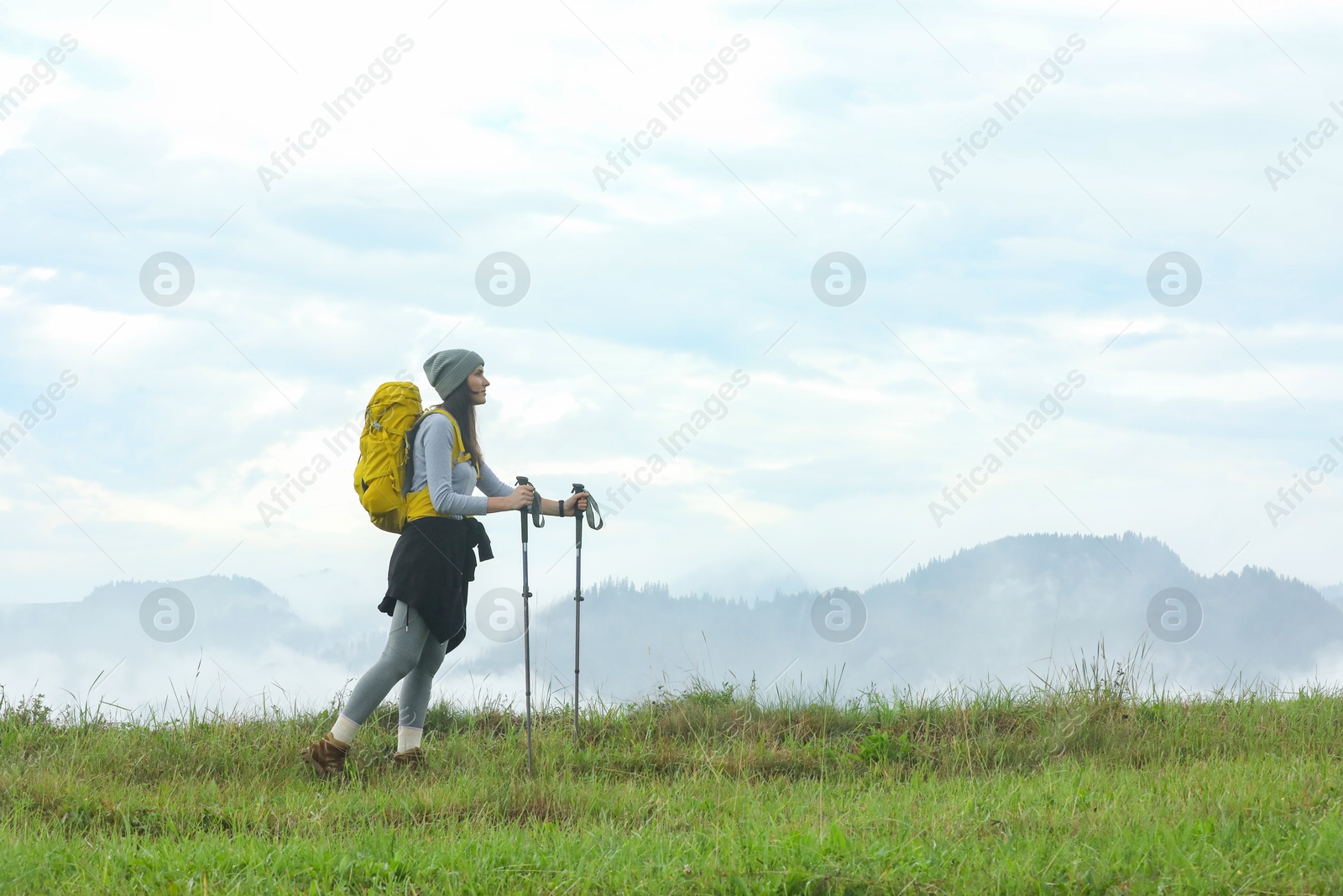 Photo of Young hiker with backpack and trekking poles in mountains, space for text