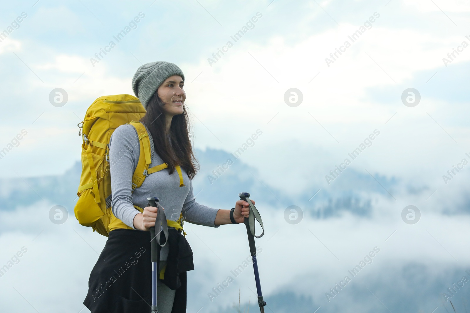 Photo of Young hiker with backpack and trekking poles in mountains, space for text