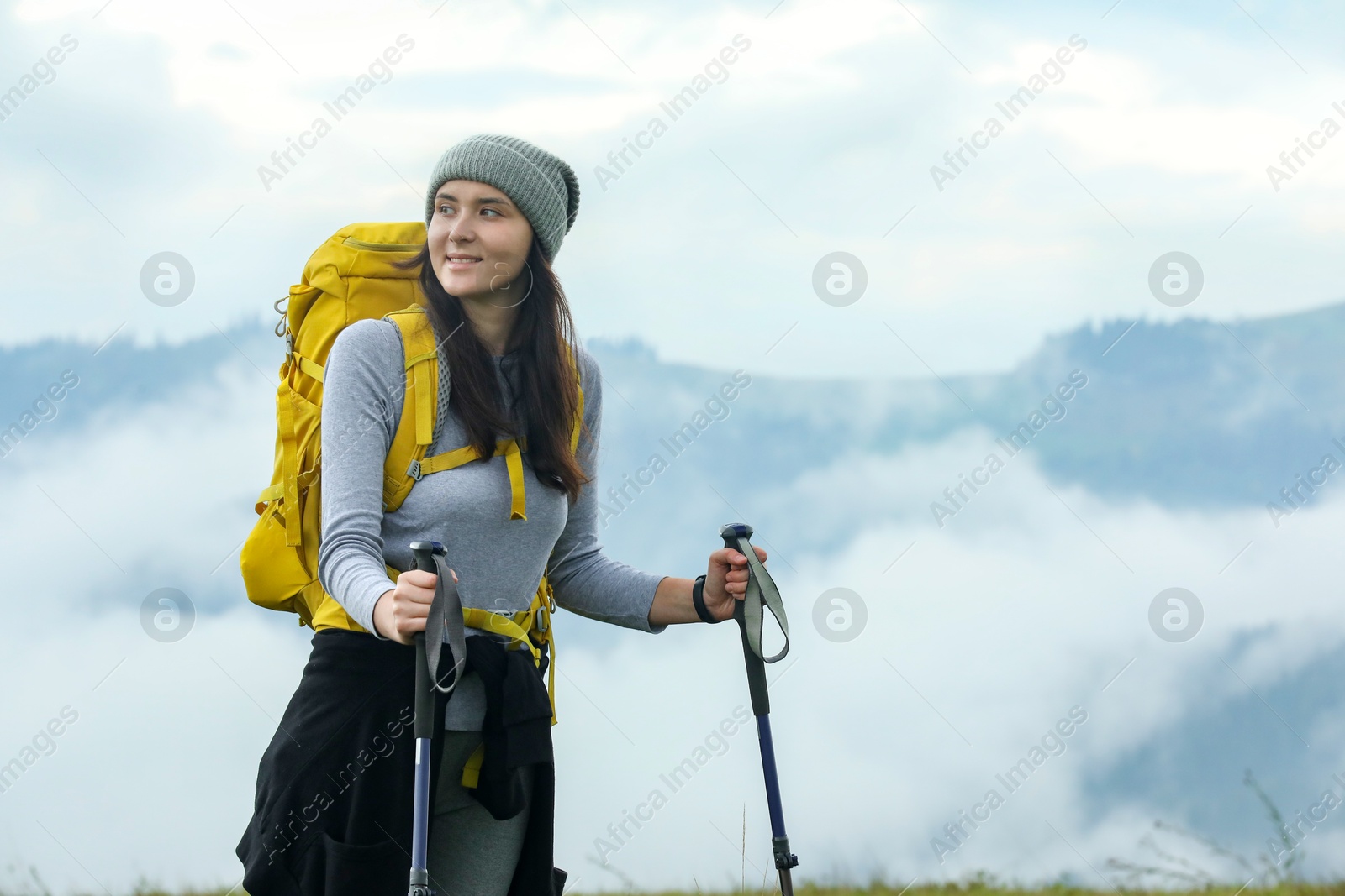 Photo of Young hiker with backpack and trekking poles in mountains, space for text