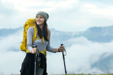 Photo of Young hiker with backpack and trekking poles in mountains, space for text