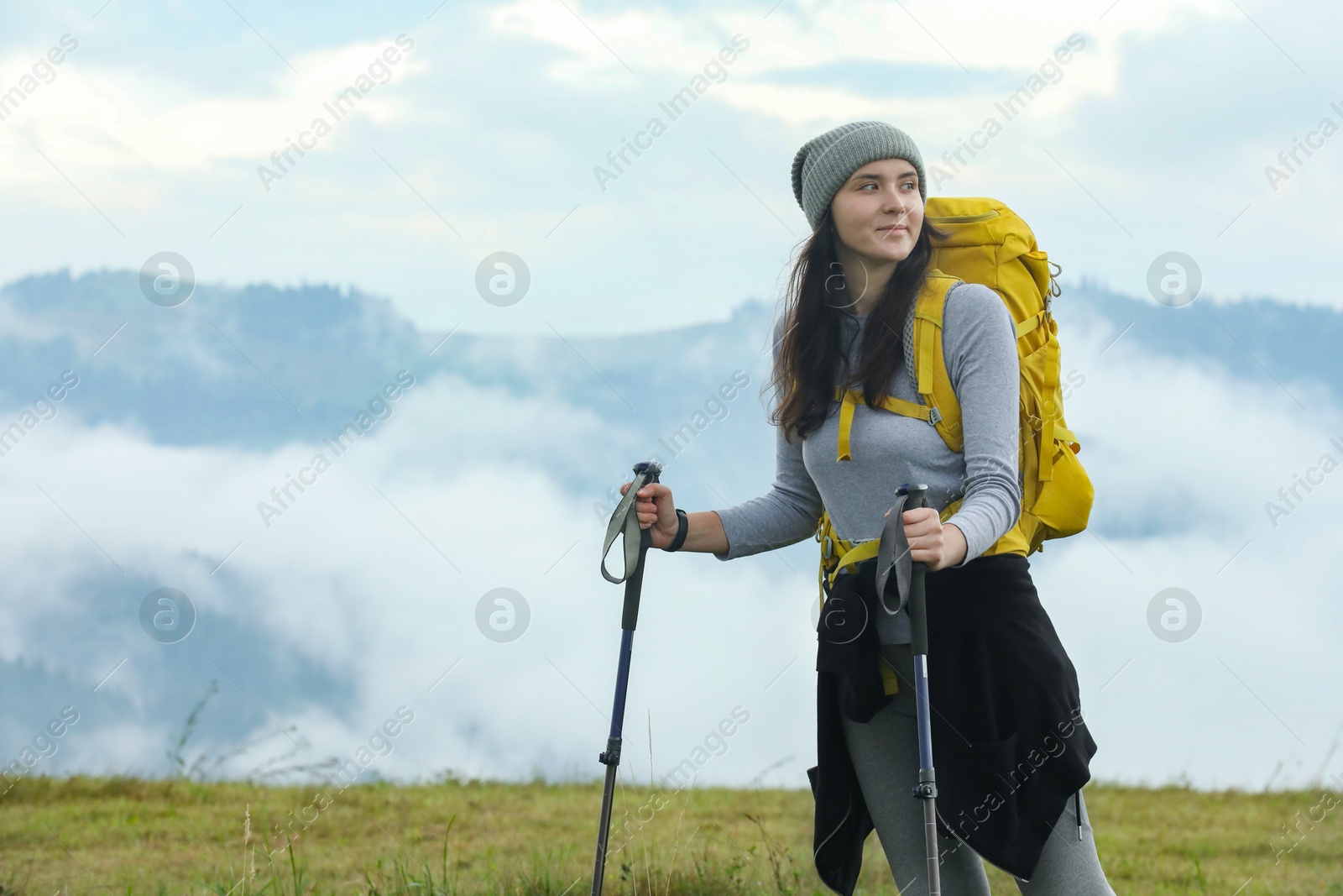 Photo of Young hiker with backpack and trekking poles in mountains, space for text