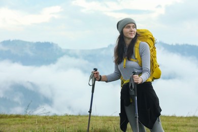 Photo of Young hiker with backpack and trekking poles in mountains, space for text