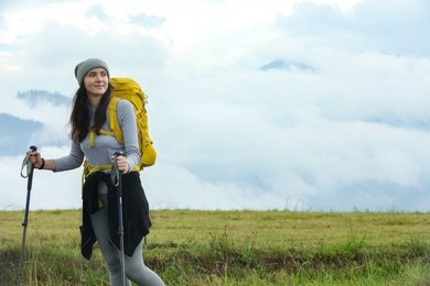 Photo of Young hiker with backpack and trekking poles in mountains, space for text