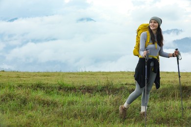 Young hiker with backpack and trekking poles in mountains, space for text