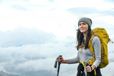 Photo of Young hiker with backpack and trekking poles in mountains, space for text