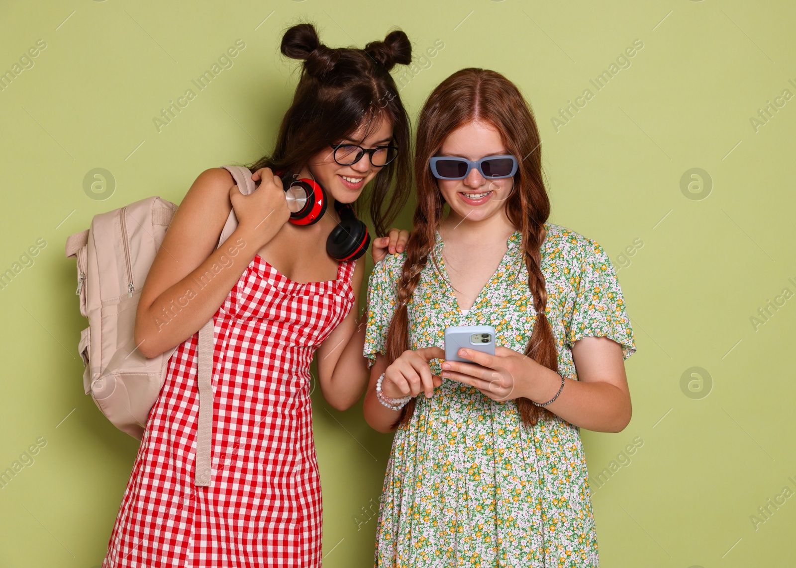 Photo of Happy teenage girls looking at smartphone on green background. Space for text