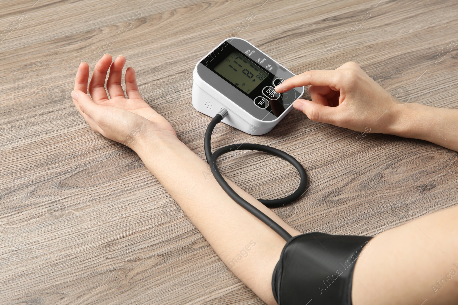 Photo of Woman measuring her blood pressure with device at wooden table, closeup