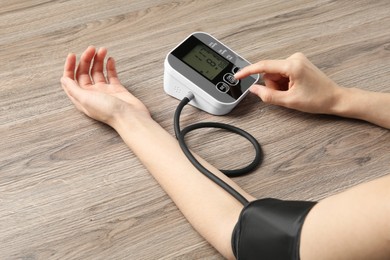 Woman measuring her blood pressure with device at wooden table, closeup