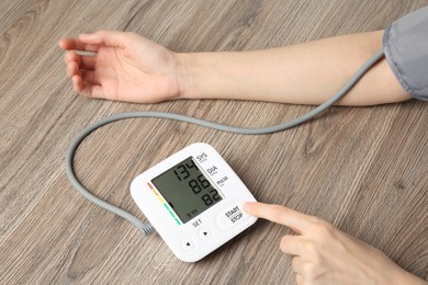 Photo of Woman measuring her blood pressure with device at wooden table, closeup