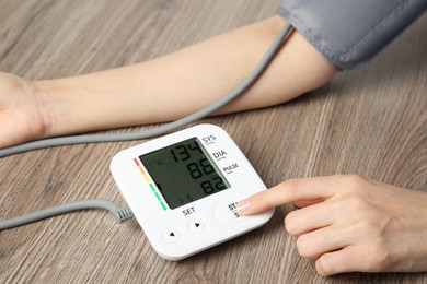 Woman measuring her blood pressure with device at wooden table, closeup