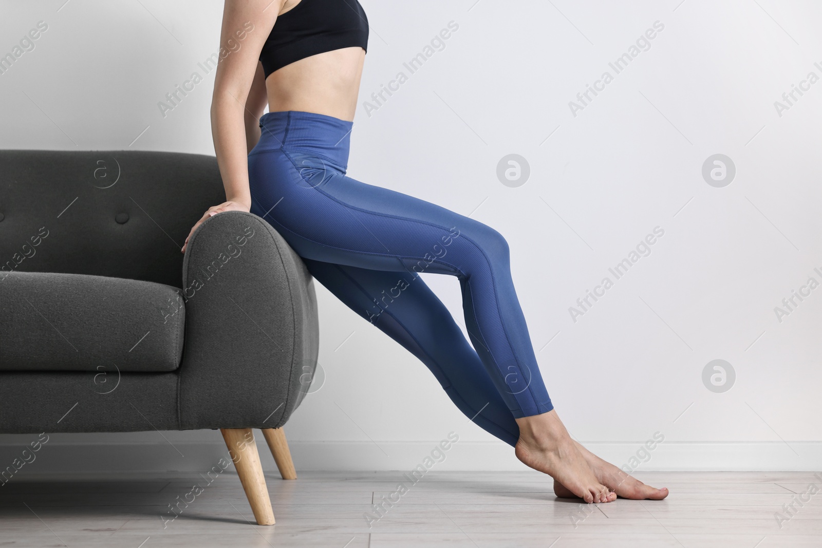 Photo of Woman wearing blue sports leggings near sofa indoors, closeup