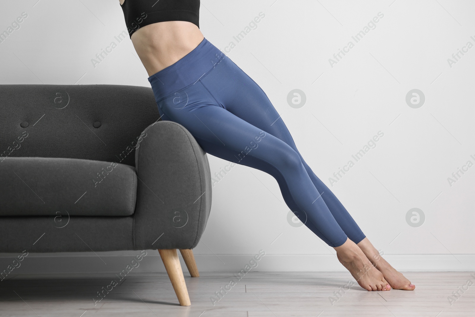 Photo of Woman wearing blue sports leggings near sofa indoors, closeup