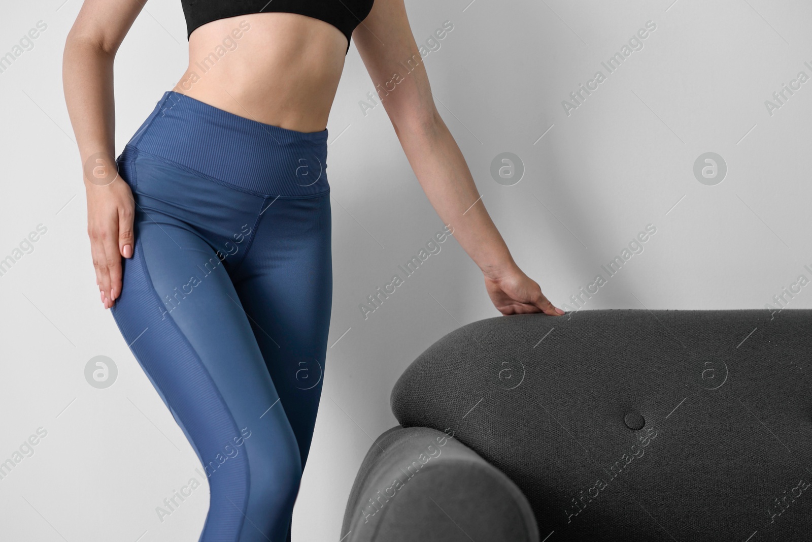 Photo of Woman wearing blue sports leggings near sofa indoors, closeup