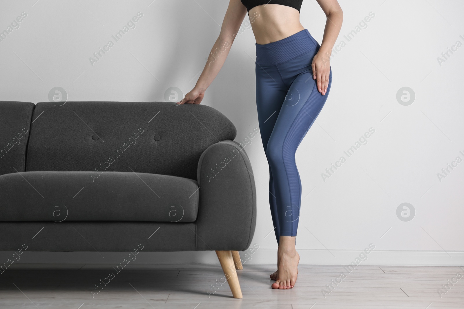 Photo of Woman wearing blue sports leggings near sofa indoors, closeup