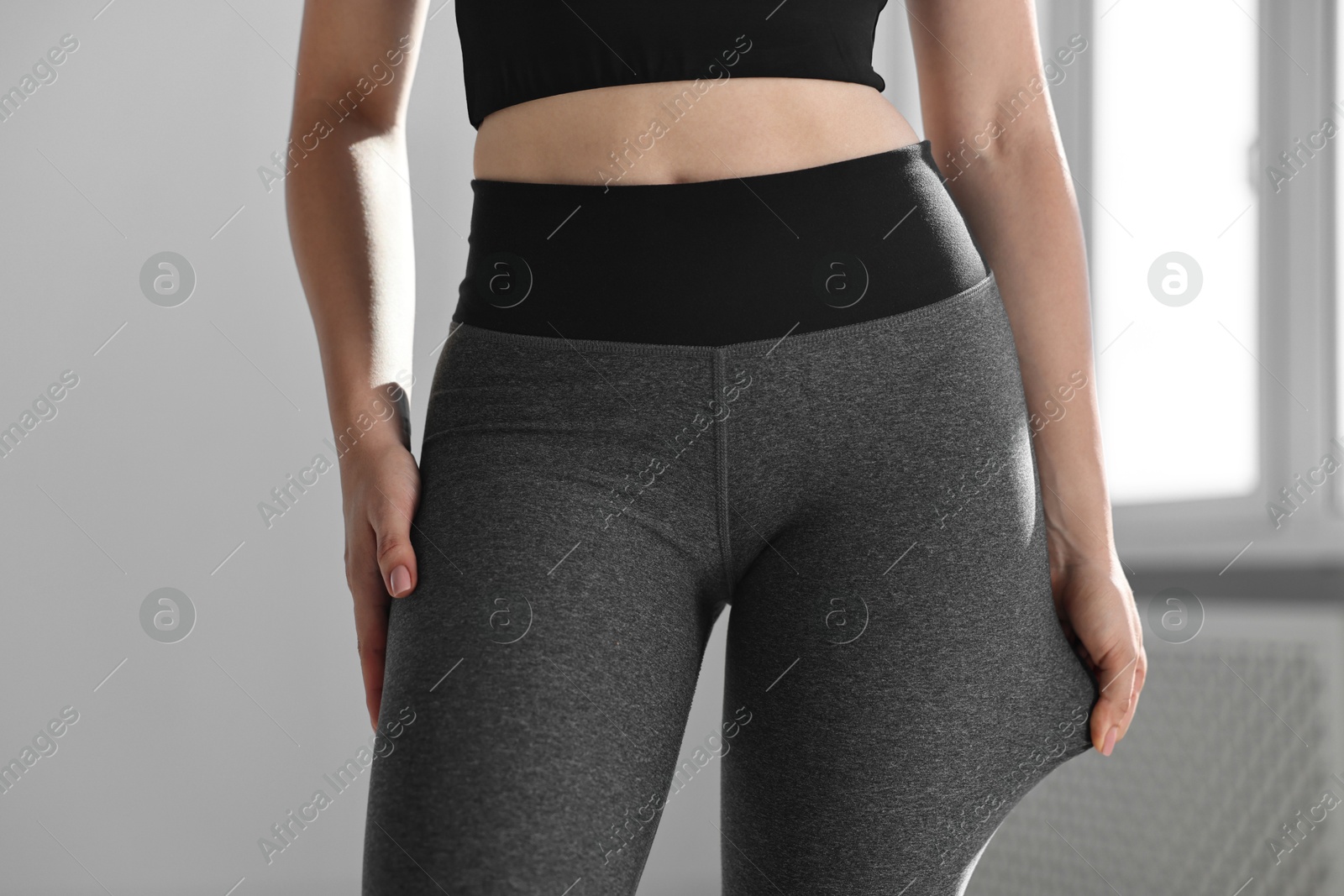 Photo of Woman wearing grey sports leggings indoors, closeup