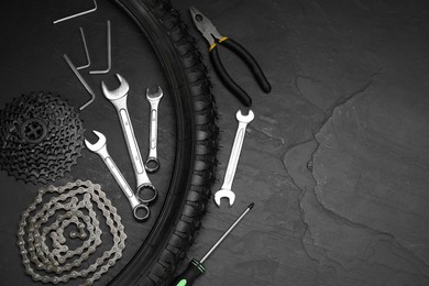 Parts of bicycle and tools on black table, flat lay. Space for text