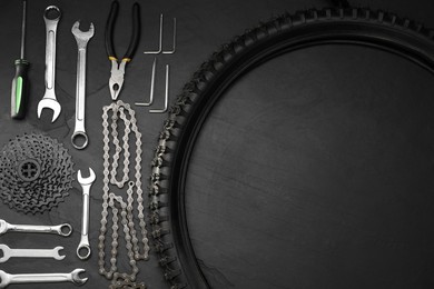 Parts of bicycle and tools on black table, flat lay. Space for text