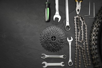 Parts of bicycle and tools on black table, flat lay. Space for text