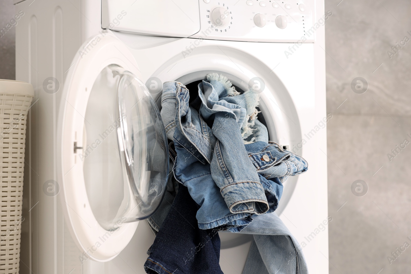 Photo of Washing machine with dirty jeans and other denim clothes indoors