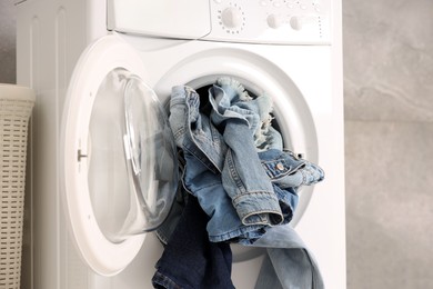 Photo of Washing machine with dirty jeans and other denim clothes indoors