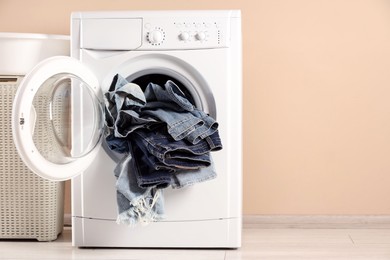 Washing machine with dirty jeans and other denim clothes indoors, space for text