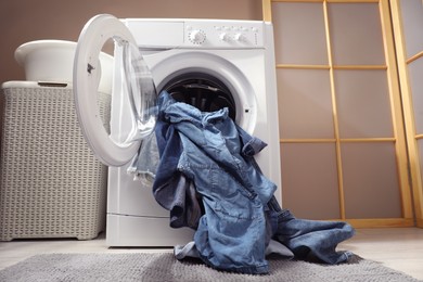 Washing machine with dirty jeans and other denim clothes indoors, low angle view