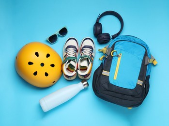 Bicycle helmet, accessories and sneakers on light blue background, flat lay