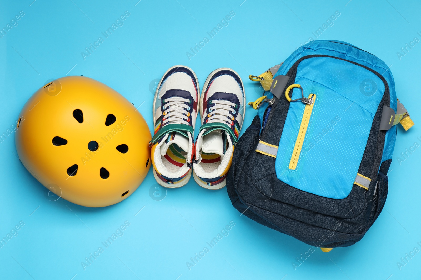 Photo of Bicycle helmet, sneakers and backpack on light blue background, flat lay