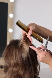 Hairdresser cutting client's hair with scissors in salon, closeup