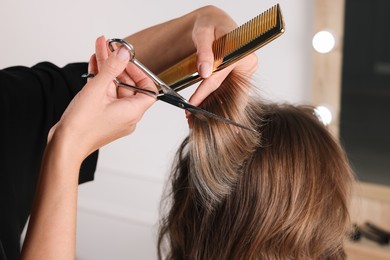 Hairdresser cutting client's hair with scissors in salon, closeup